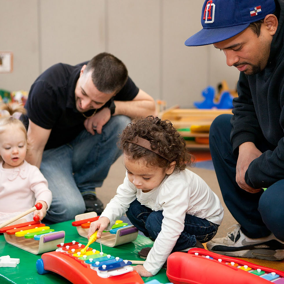 A photo of two male caregivers interacting with two toddlers who are playing with musical instruments.