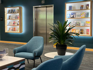 Three chairs are arranged around tables creating a reading area. The elevator doors and display shelves from on the second floor are in the background.