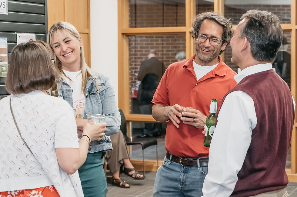 A group of smiling people, facing the camera, two with their backs to the camera, have a lighthearted conversation