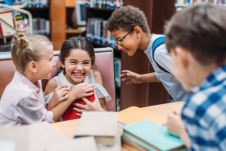 Four smiling and laughing children are gathered around a table filled with books.