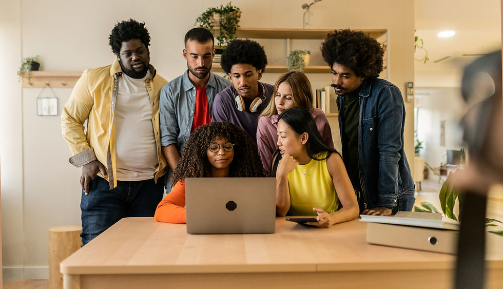 A group of people stand around a woman working on a laptop