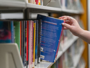 A person reaches in from out of frame to pull a book off a full shelf.