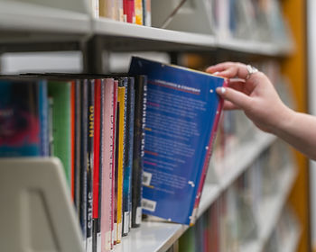 A person reaches in from out of frame to pull a book off a full shelf.