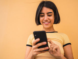 A woman with short dark hair smiles as she uses a smartphone.