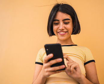 A woman with short dark hair smiles as she uses a smartphone.