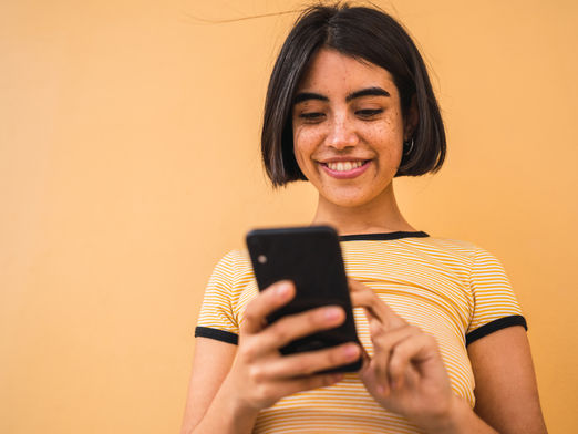 A woman with short dark hair smiles as she uses a smartphone.