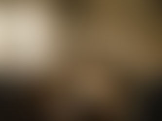 An photographic image looking over the shoulder of a out-of-focus person with their back to the camera, off to the right side of the image. They look at a pile of moving boxes in a older, dusty apartment. 