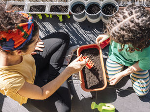 A woman and a child plant seeds in a container on a balcony.