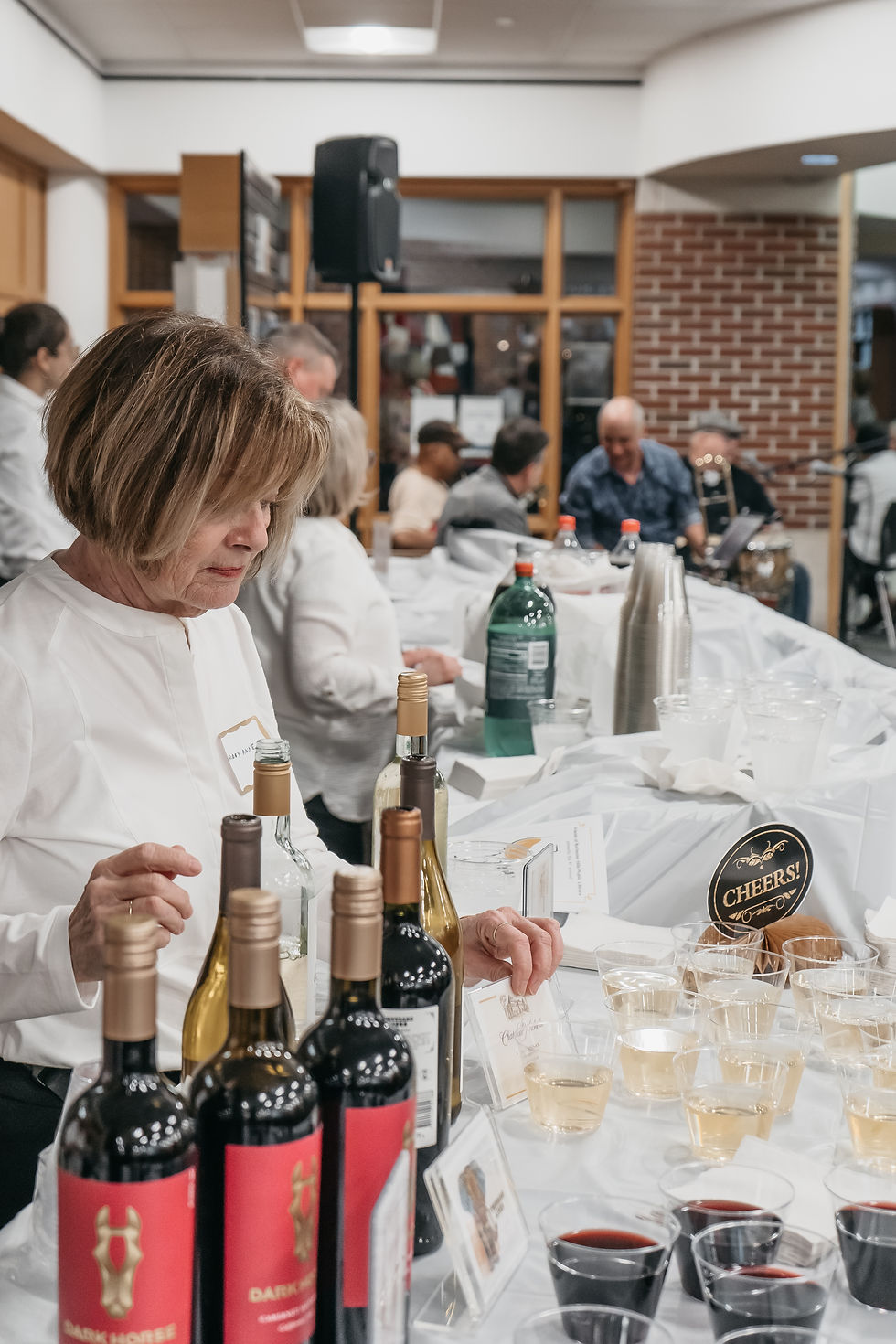 A woman attends a bar, setting out pre-filled white and red wine glasses, with the bottles set behind them.