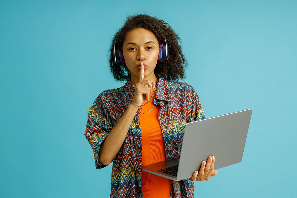 A woman holding a laptop has her finger infront of her lips in a "shhh" gesture