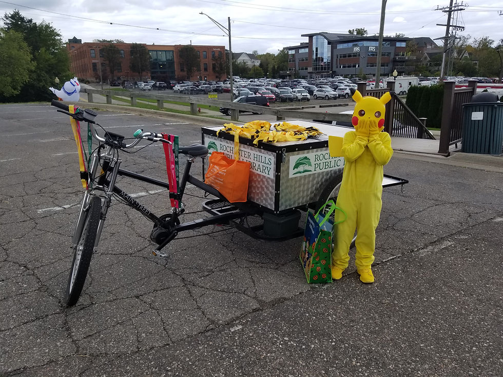 A kid dressed as Pikachu stands next to the Book Bike at Halloween Fest.