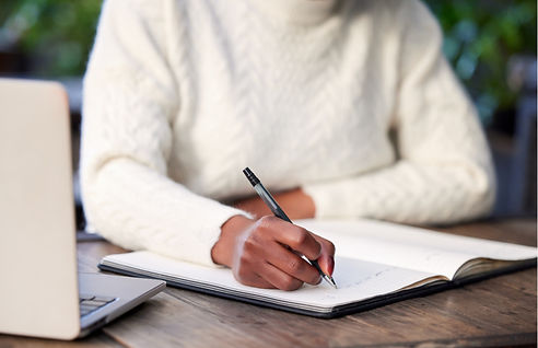 A person writes in a notebook next to an open computer