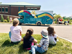 A group of four kids sits in the foreground, looking at the blue bus in the background.