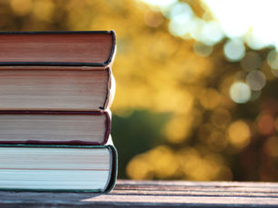 A stack of books is silhouetted against a background of fall trees.