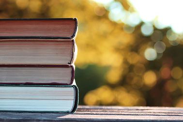 A stack of books is silhouetted against a background of fall trees.