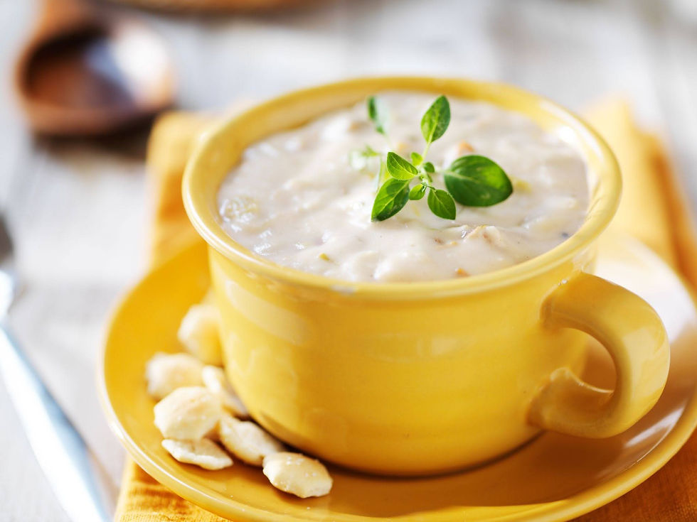 Clam chowder in a yellow mug and saucer, topped with English Thyme and served with a small handful of oyster crackers on the saucer.