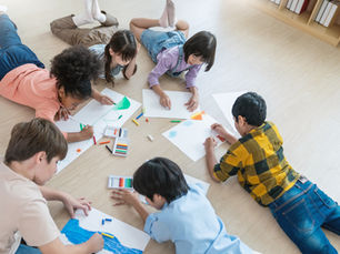 A group of children lies on a wood floor drawing pictures.