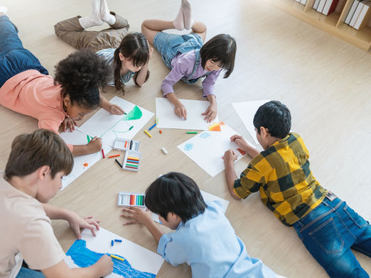 A group of children lies on a wood floor drawing pictures.