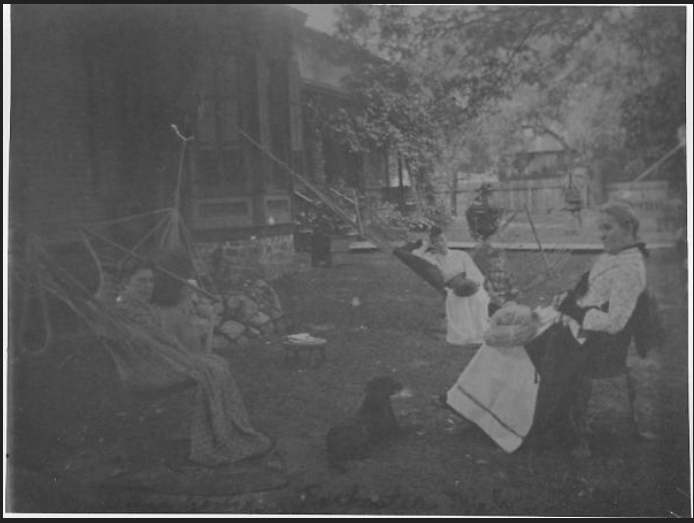 A historical black and white photograph of three women in the yard of a home, two relaxing in hammocks, looking at the camera, and one in a chair in profile.