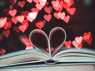 An open book with the page in the shape of a heart, with red and pink overlapping hearts in the background
