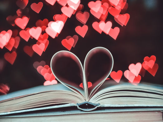 An open book with the page in the shape of a heart, with red and pink overlapping hearts in the background 