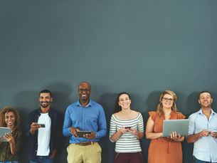 A group of smiling people holding different devices
