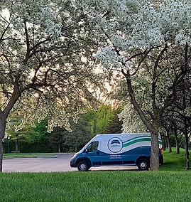A photo of the RHPL bookmobile parked in the parking lot under an apple tree in full bloom in springtime.