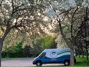 A photo of the RHPL bookmobile parked in the parking lot under an apple tree in full bloom in springtime.