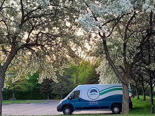 A photo of the RHPL bookmobile parked in the parking lot under an apple tree in full bloom in springtime.