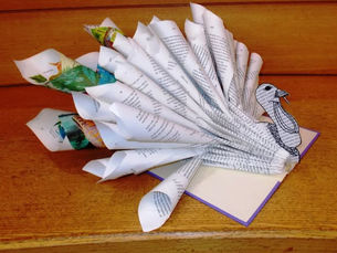 The pages of an open hardcover book are curled inward, folded, and cut to resemble various parts of a turkey sticking out from the inside spine