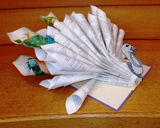 The pages of an open hardcover book are curled inward, folded, and cut to resemble various parts of a turkey sticking out from the inside spine