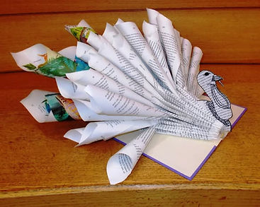 The pages of an open hardcover book are curled inward, folded, and cut to resemble various parts of a turkey sticking out from the inside spine