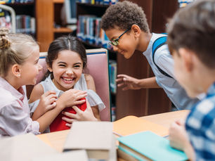 Four smiling and laughing children are gathered around a table filled with books.