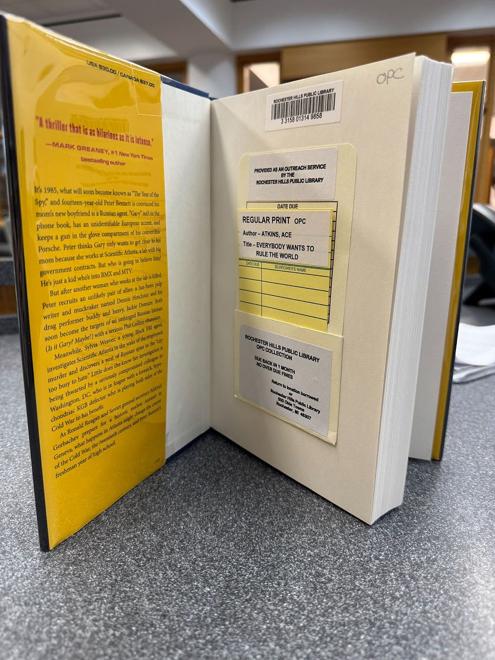 A picture of the inside cover of an RHPL book from the OPC mini-branch. The label says "Provided as an outreach service by the Rochester Hills Public Library" There are other labels detailing the title of the book and the location of the book, the checkout period, and the fact that there are no overdue fines.