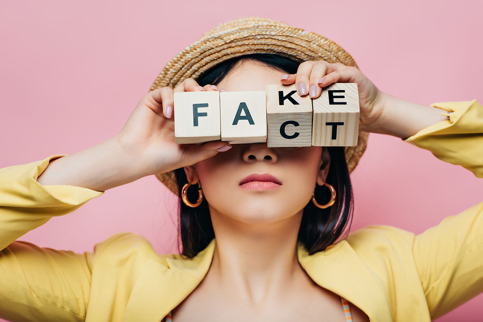 A woman holding four blocks in front of her face that spell "fake" and "fact" depending on which way they are held.