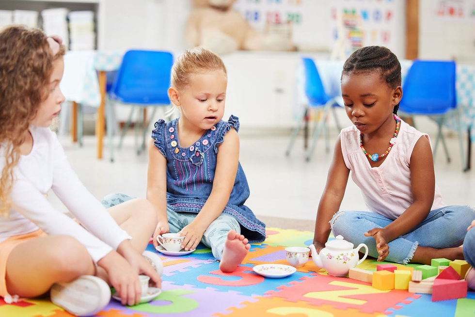 Three children sit on the floor with play teacups and a teapot