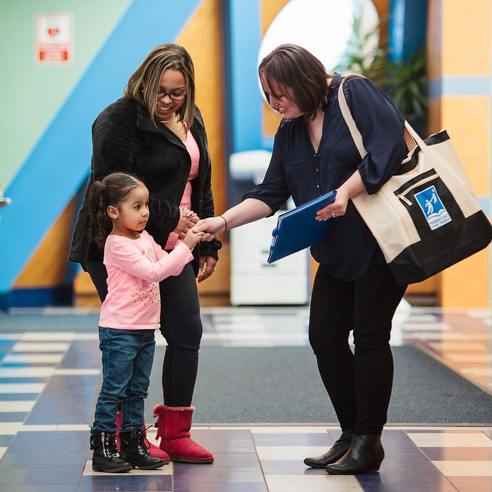 A woman shakes the hand of a preschooler while her female caregiver smiles down at her and holds her other hand.