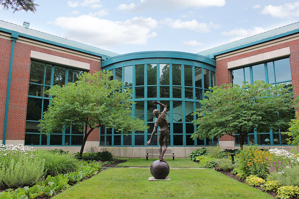 A statue of a boy balancing on a ball with RHPL's gardens and large windows