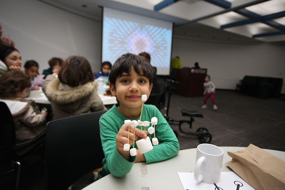 A child holds up a snowflake made of marshmallows and toothpicks