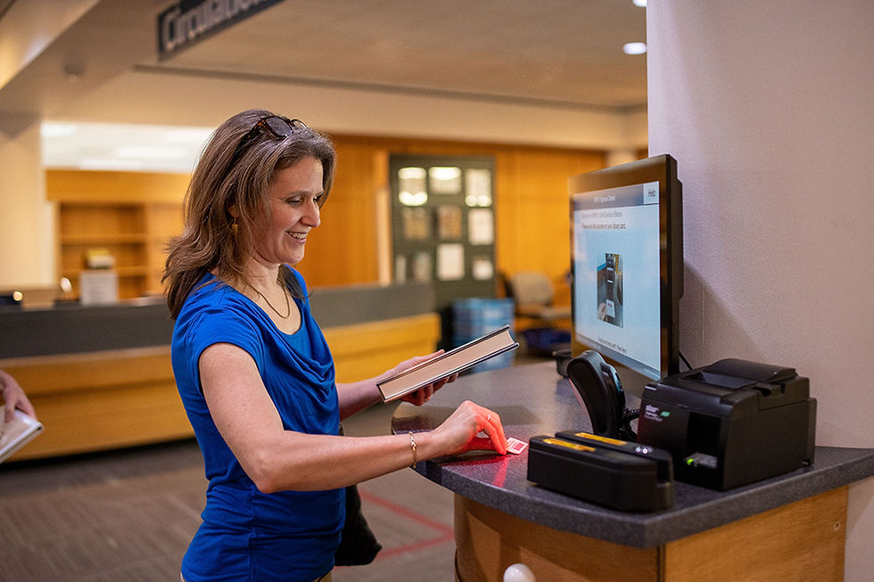 A smiling woman scans her library card at the self check out machine