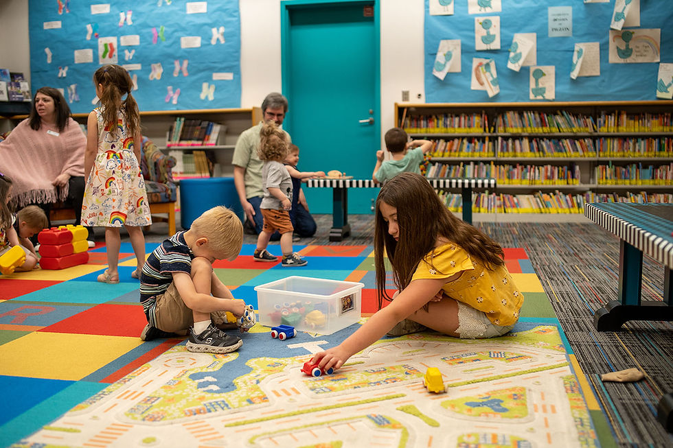 A young boy and girl play with toy cars on colorful carpet in the Youth Services' Explorer Zone