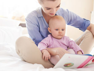 A young woman and her infant sit reading a book together