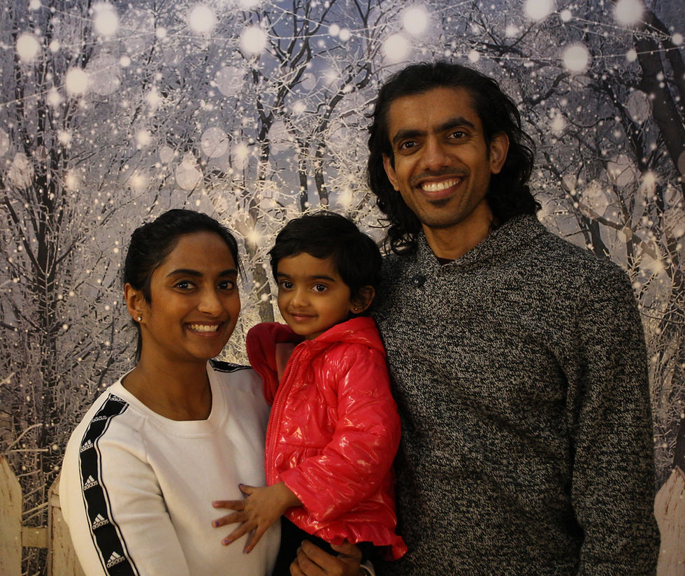 A woman, man, and little girl pose for a picture with a wintery backdrop behind them.